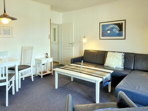 Ein Wohnzimmer mit Sofa, Sesseln, Couchtisch, Lampe und einer Tür.