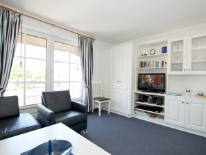 Ein Wohnzimmer mit einer Couch, einem Fernseher und weißen Schränken mit Glastüren.