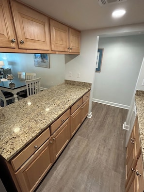 A kitchen with wooden cabinets, granite countertops, and a dining area with a table and chairs. - Ocean View, Golf Cart Included, Pet Friendly, Walk to the Beach - 406 Captain John Fripp Villa (Fripp Island)