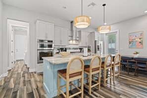 A modern kitchen with white cabinetry, a central island with bar stools, and pendant lighting. - East Austin Twin-Home Retreat w/ Kids` Play Area & String-Lit Courtyard (Austin)