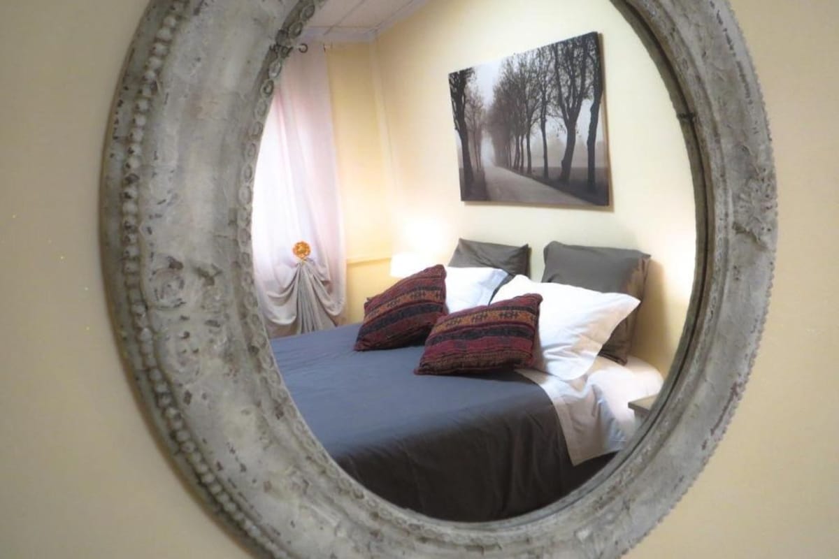 Una camera da letto con un letto, cuscini, un comodino e un quadro appeso al muro.