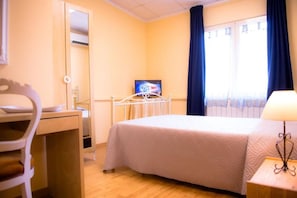 A hotel room with a bed, a desk, a chair, a TV, and a window with curtains.