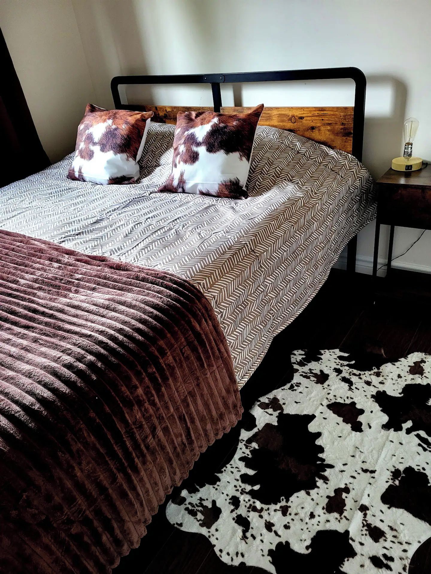A bed with patterned bedding, two pillows, a brown blanket, and a cowhide rug.