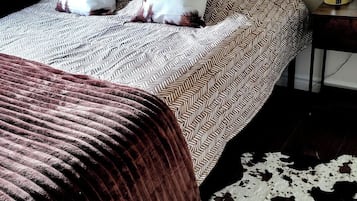 A bed with patterned bedding, two pillows, a brown blanket, and a cowhide rug.