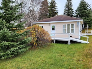 Une petite cabane à un seul étage, dotée d’un porche à l’avant et d’une rampe d’accès pour les personnes à mobilité réduite.