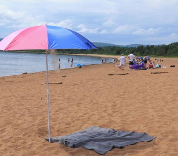 Une plage avec un grand parasol, des gens et une couverture sur le sable.