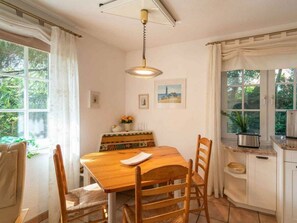 Ein Essbereich mit Holztisch und Stühlen, einer Hängeleuchte und Blick ins Freie durch große Fenster.