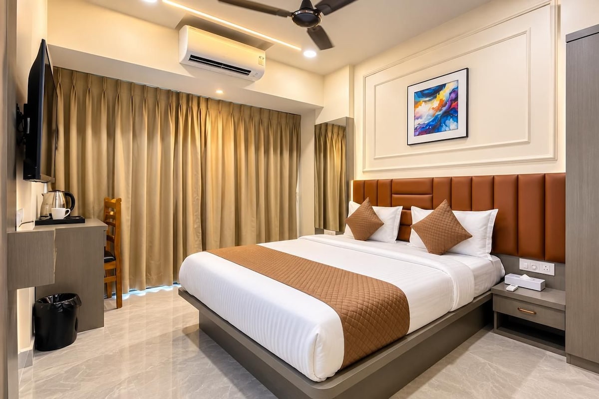 A hotel room with a bed, bedside table, TV, air conditioning unit, and a painting on the wall.