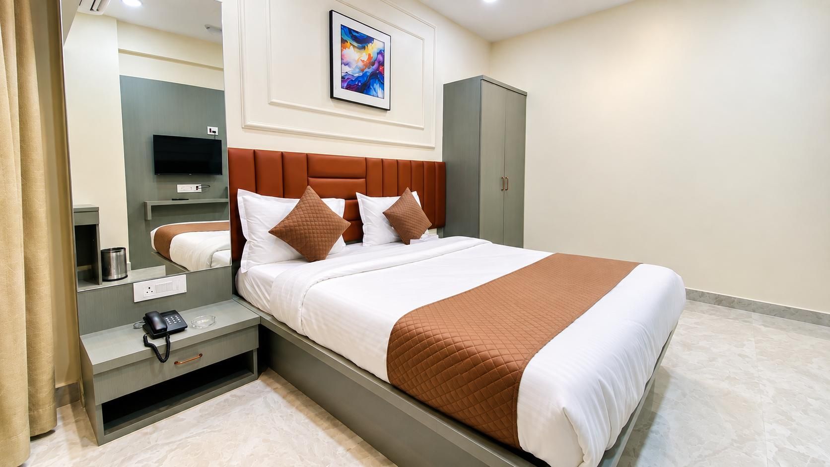 Una habitación de hotel con cama, mesita de noche, lámpara y televisor.