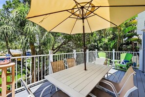 Um pátio externo com mesa, cadeiras, um guarda-sol grande e um cercado branco.