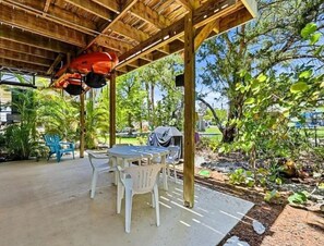 Eine überdachte Terrasse im Freien mit Tisch und Stühlen, umgeben von Grünpflanzen und Bäumen.