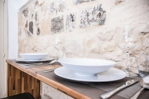 Une table à manger dressée avec de l’assiette blanche, des bols et des couverts, le tout placé devant un mur en pierre.