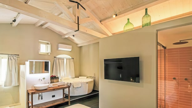 Habitación de hotel con cama, tocador con espejo, bañera, televisión montada en la pared y zona de ducha.