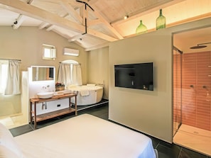 Une chambre d’hôtel comprenant un lit, une coiffeuse avec un miroir, une baignoire, un téléviseur fixé au mur et un espace douche.