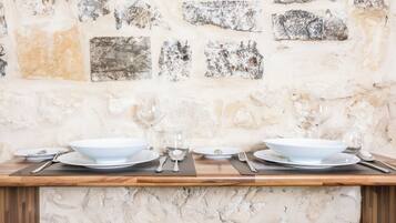 A dining table set with white plates, bowls, and cutlery against a stone wall.