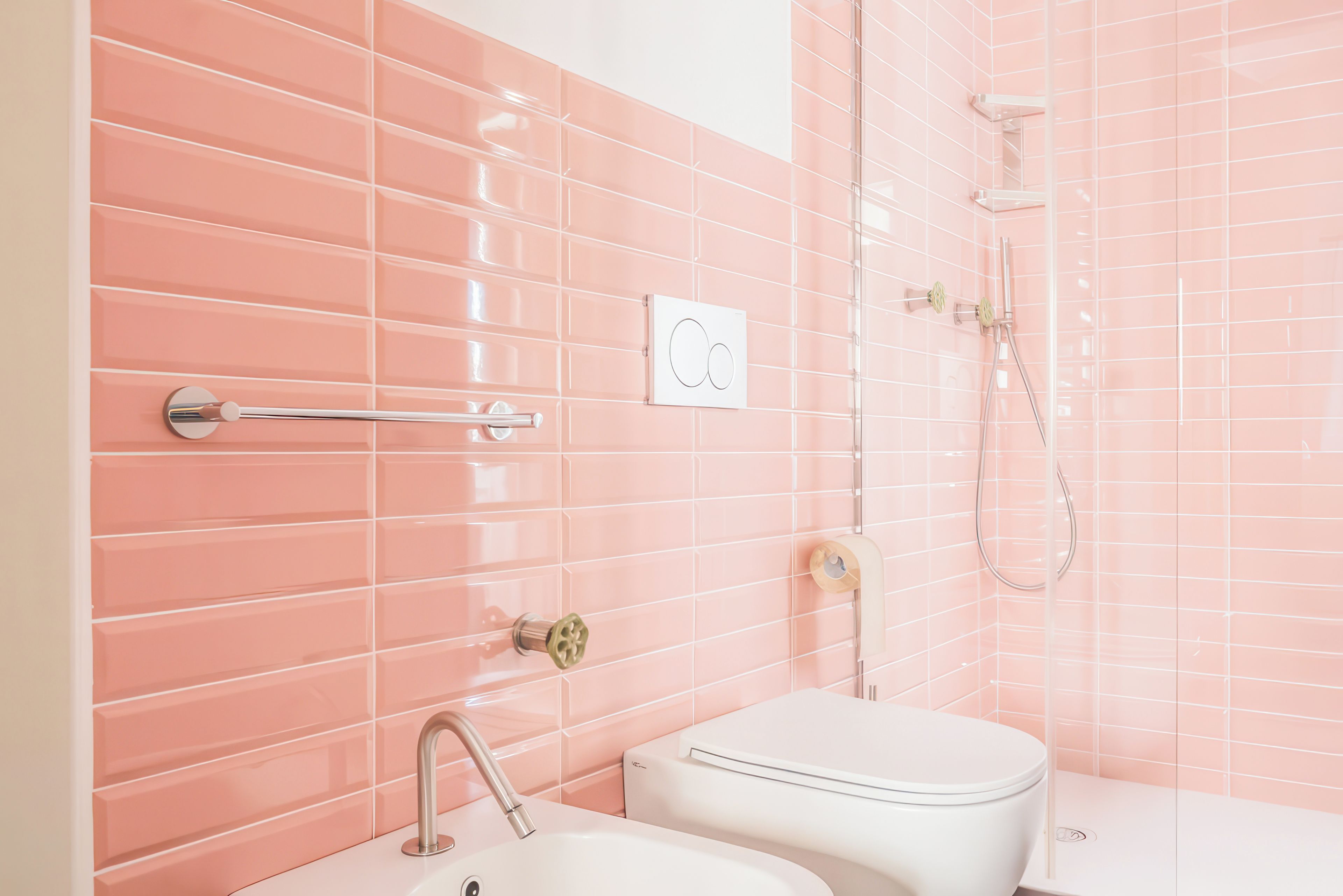 A bathroom with pink tiled walls, a white toilet, a sink, and a shower.