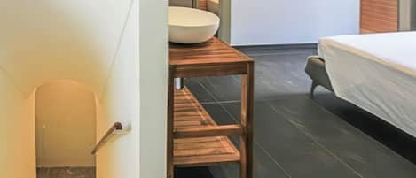 A modern bathroom with a white sink, wooden vanity, and a bed with a white cover.