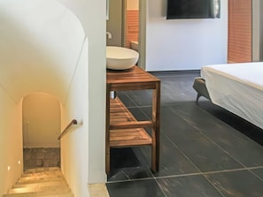 Une salle de bain moderne avec un lavabo blanc, un meuble-lavabo en bois et un lit recouvert d’une couverture blanche.