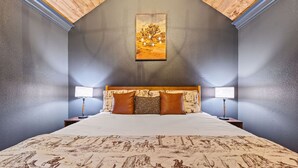 Een slaapkamer met een groot bed, twee bedlampjes, een schilderij aan de muur en een schuine plafond.