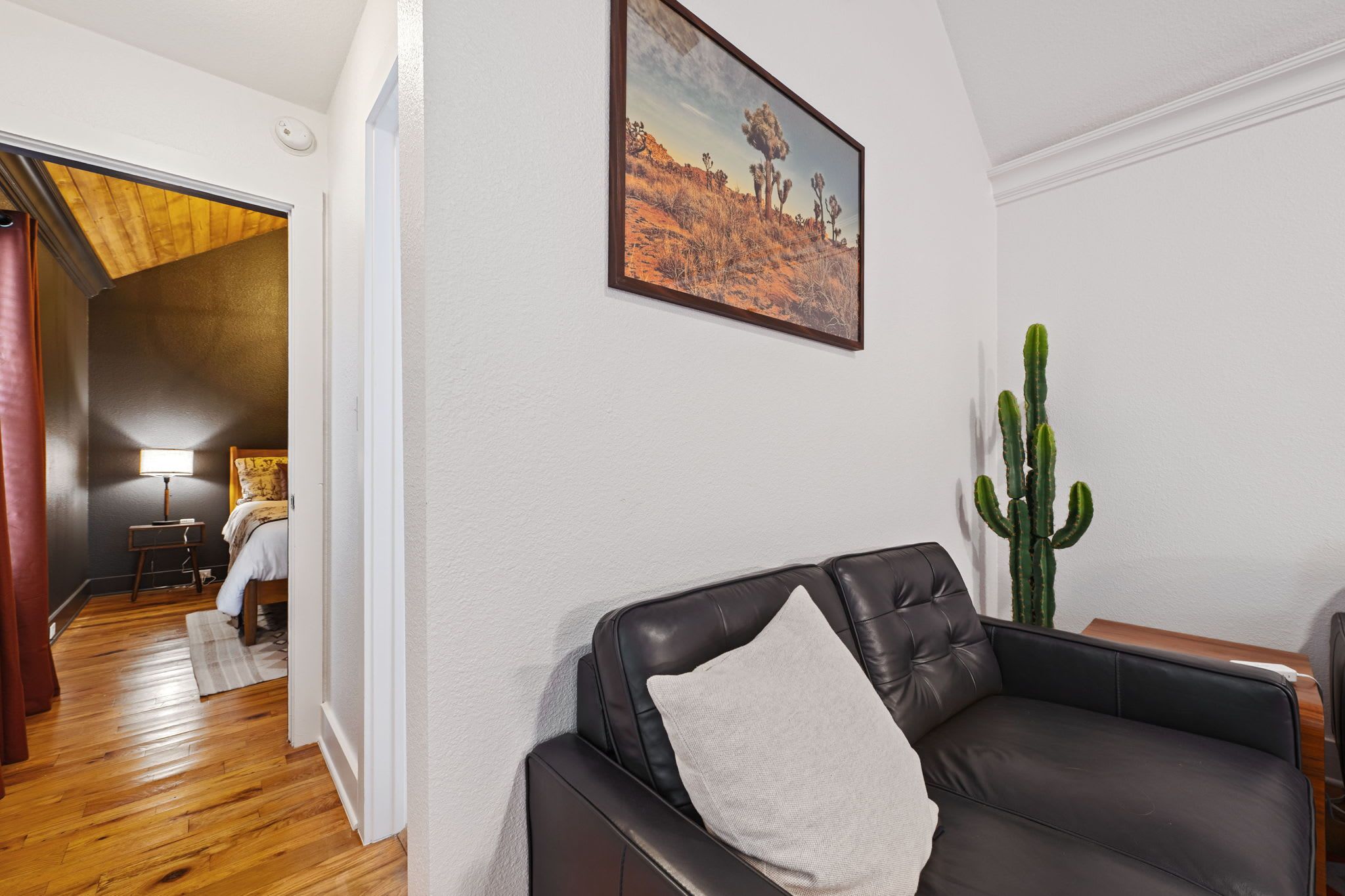 A living room with a black leather sofa, a cactus plant, and a painting of a desert landscape.