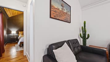 A living room with a black leather sofa, a cactus plant, and a painting of a desert landscape.