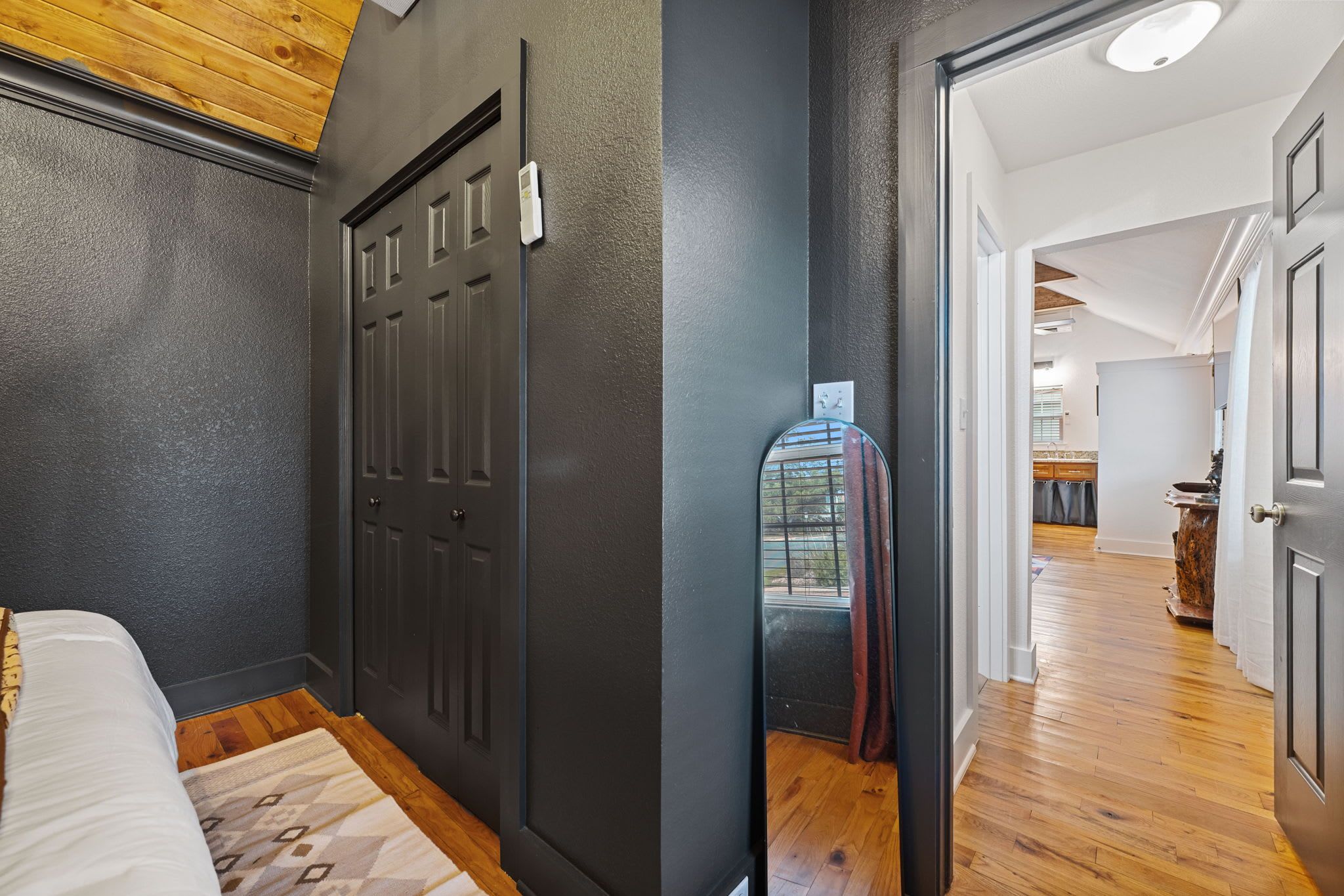 A bedroom with a bed, a dark door, and a hallway leading to a bathroom with a glass shower.