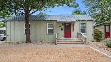 A single-story building with a red door, a small porch, and a tree in front.