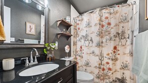 Een badkamer met een zwart wastafelmeubel, een witte wasbak, een spiegel, een toilet en een douchegordijn met een bloemenmotief.