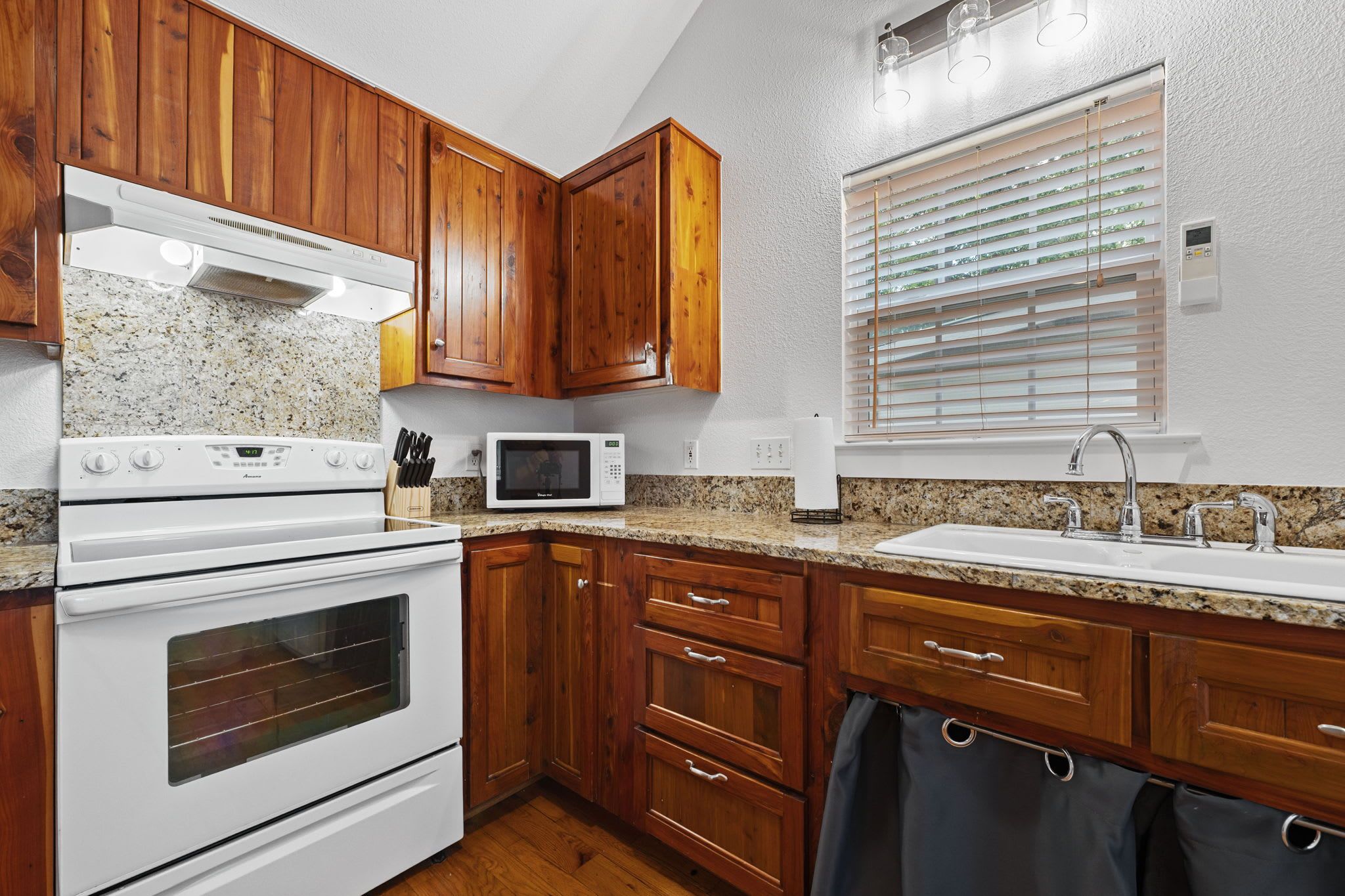 A kitchen with wooden cabinets, a white stove, a microwave, and a window with blinds.
