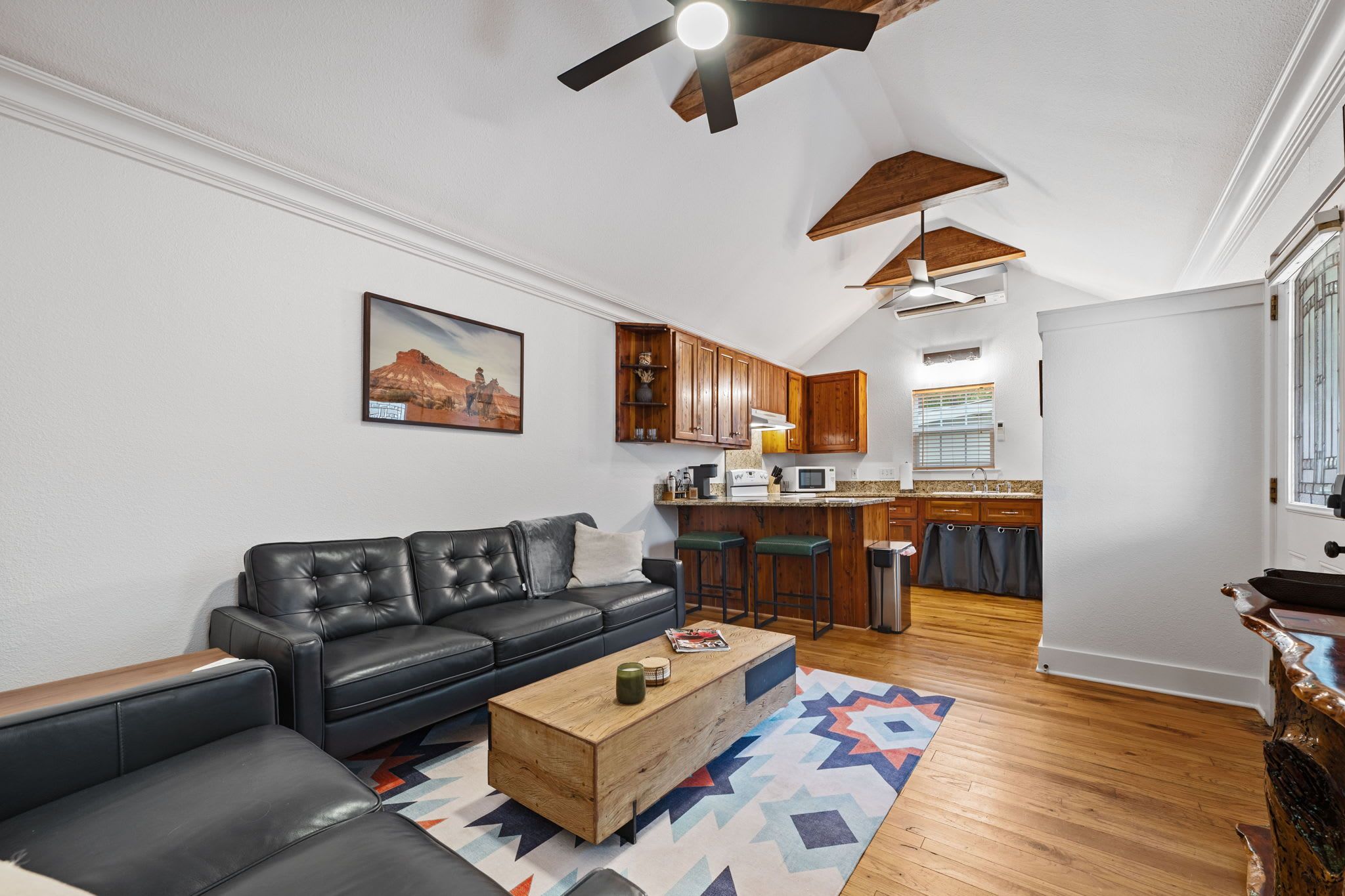 A modern living room with a black leather sofa, a wooden coffee table, and a colorful rug.
