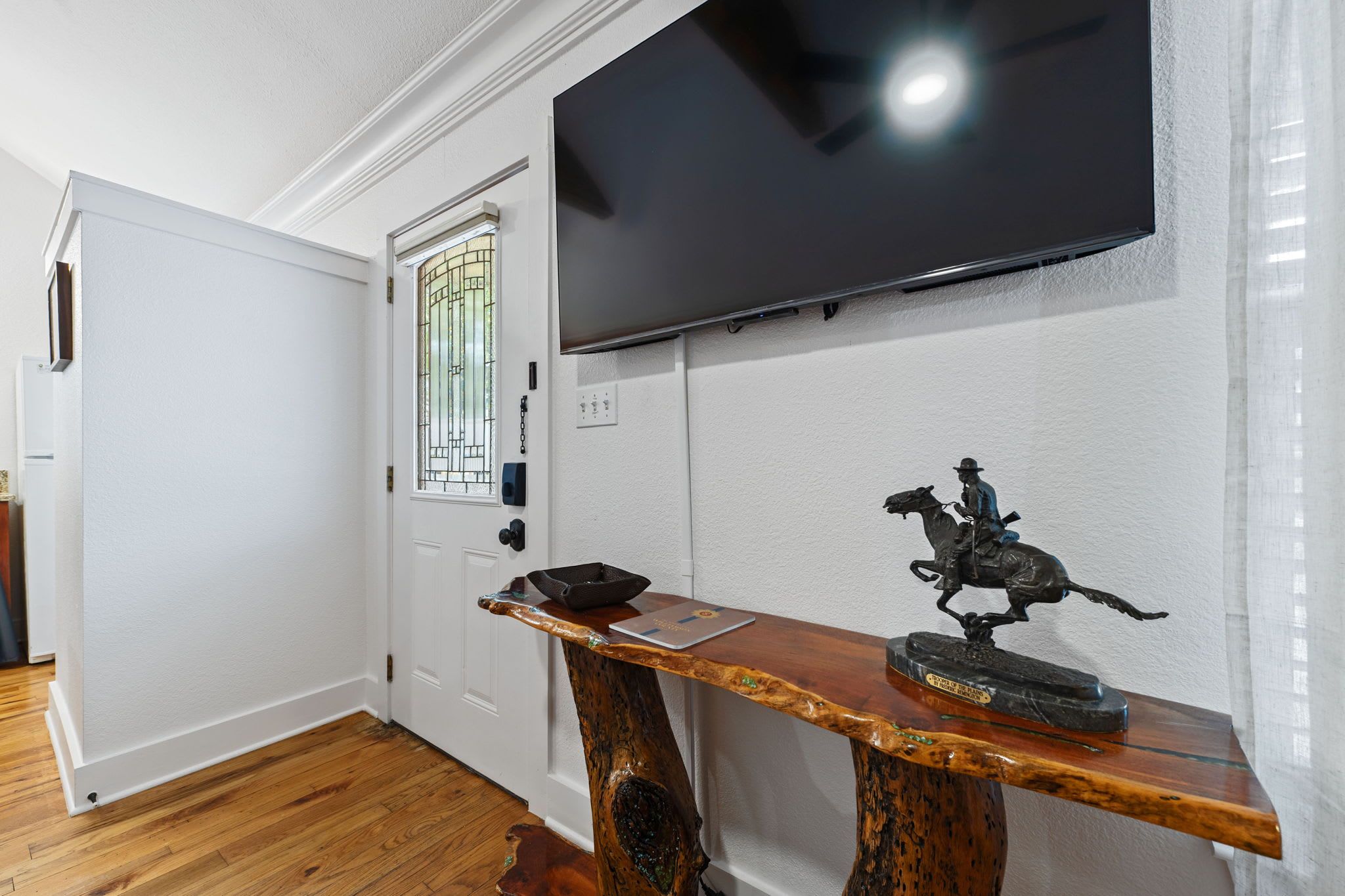 A room with a wooden table, a mounted television, and a door with a stained glass window.
