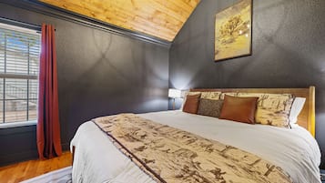 Een slaapkamer met een groot bed, een raam met gordijnen, een hoofdbord met kussens en een schilderij aan de muur.
