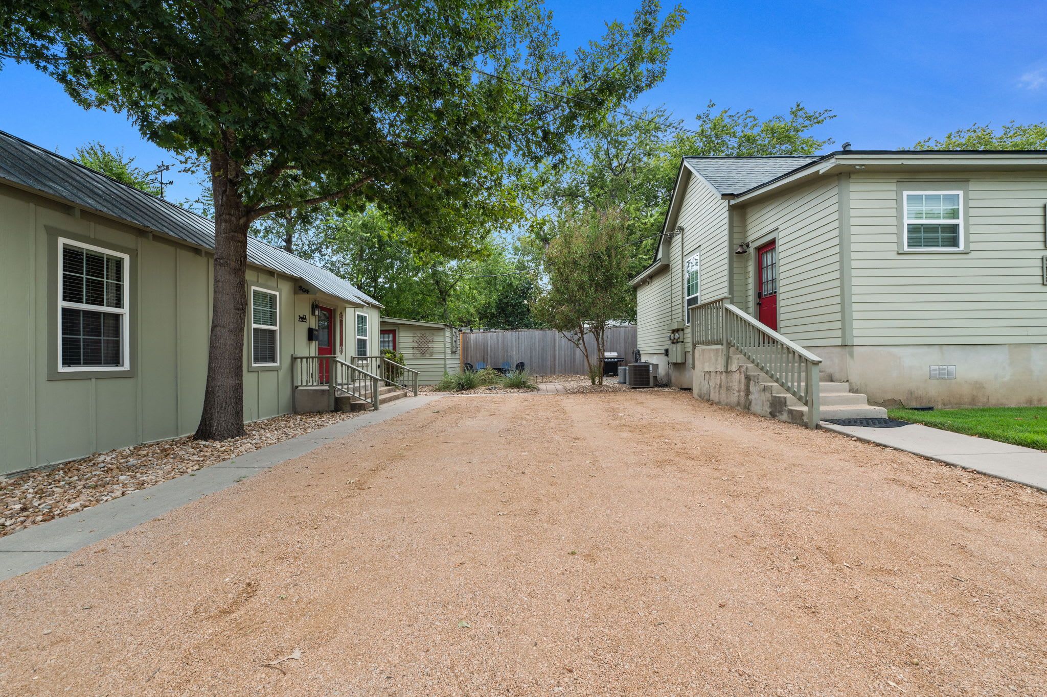 A residential area with two houses, a gravel driveway, and a wooden fence.