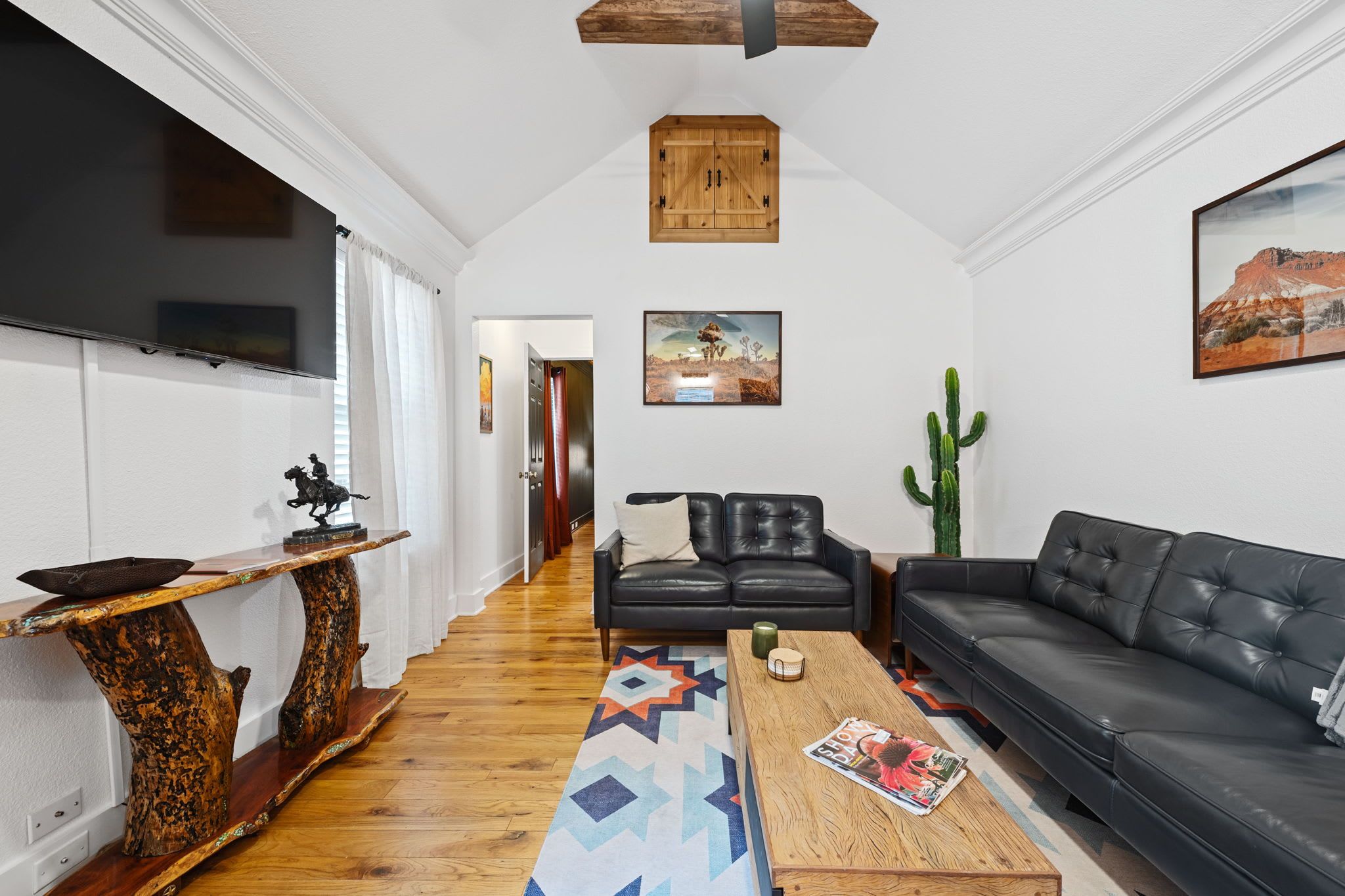 A modern living room with a wooden coffee table, a black leather sofa, and a mounted TV.