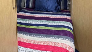 Un espacio interior compacto y bien iluminado con una cama, un ventanal y una lámpara en el techo.