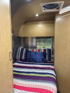 A compact, well-lit interior with a bed, a window, and a ceiling light fixture. - Moon Base Airstream | Stargazing Escape (Coryell County)