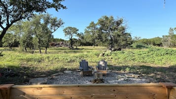 A wooden bench with two Adirondack chairs facing a natural landscape with trees and a clear sky.