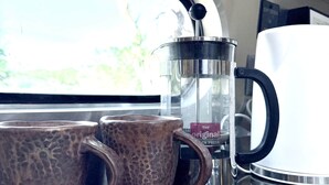 Una cafetera con jarra de vidrio y dos tazas de cerámica sobre una encimera.