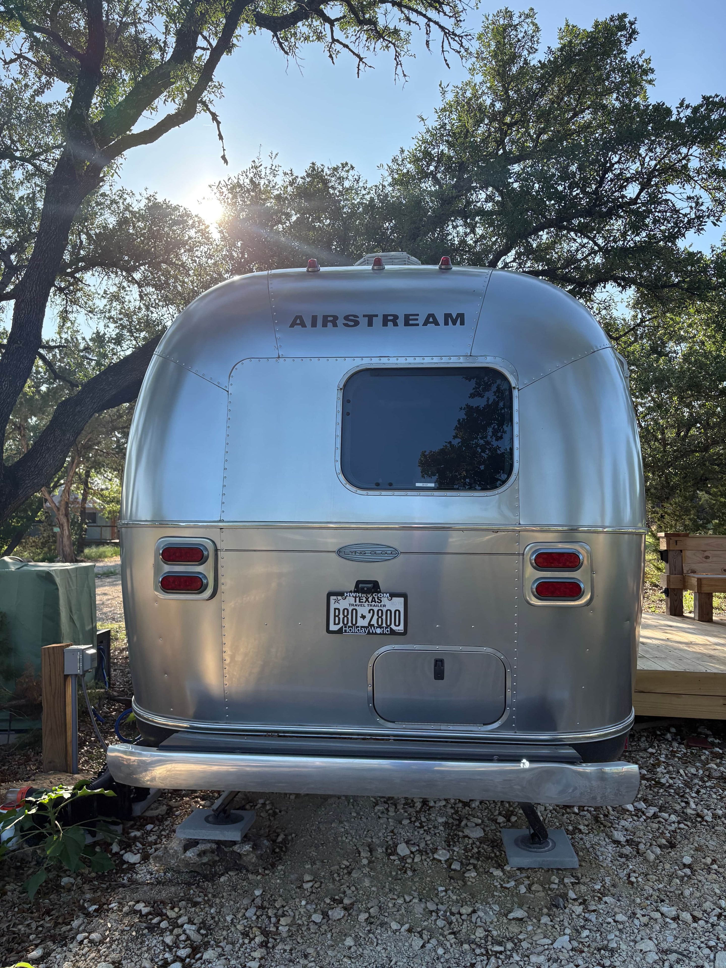 Uma caravana AIRSTREAM prateada com placa do Texas, uma pequena janela e duas luzes traseiras vermelhas.