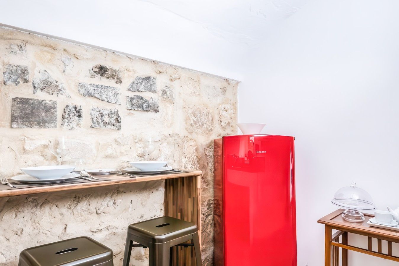 Une cuisine avec un mur en pierre, un réfrigérateur rouge et une table en bois, accompagnée de tabourets de bar.