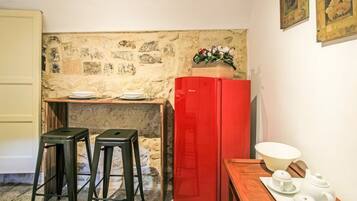 Une cuisine compacte avec un réfrigérateur rouge, deux tabourets, une table en bois avec un service à thé et un mur en pierre.