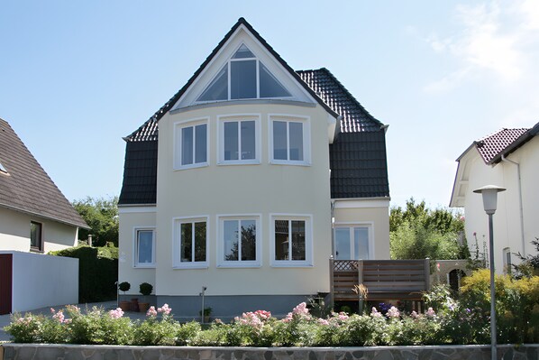 Ein zweistöckiges Haus mit Satteldach, zahlreichen Fenstern und einer Steinsäule im Vordergrund.