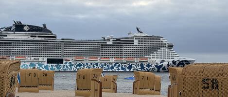 A cruise ship docked at a port with beach chairs numbered 73, 78, 70, 74, and 58.