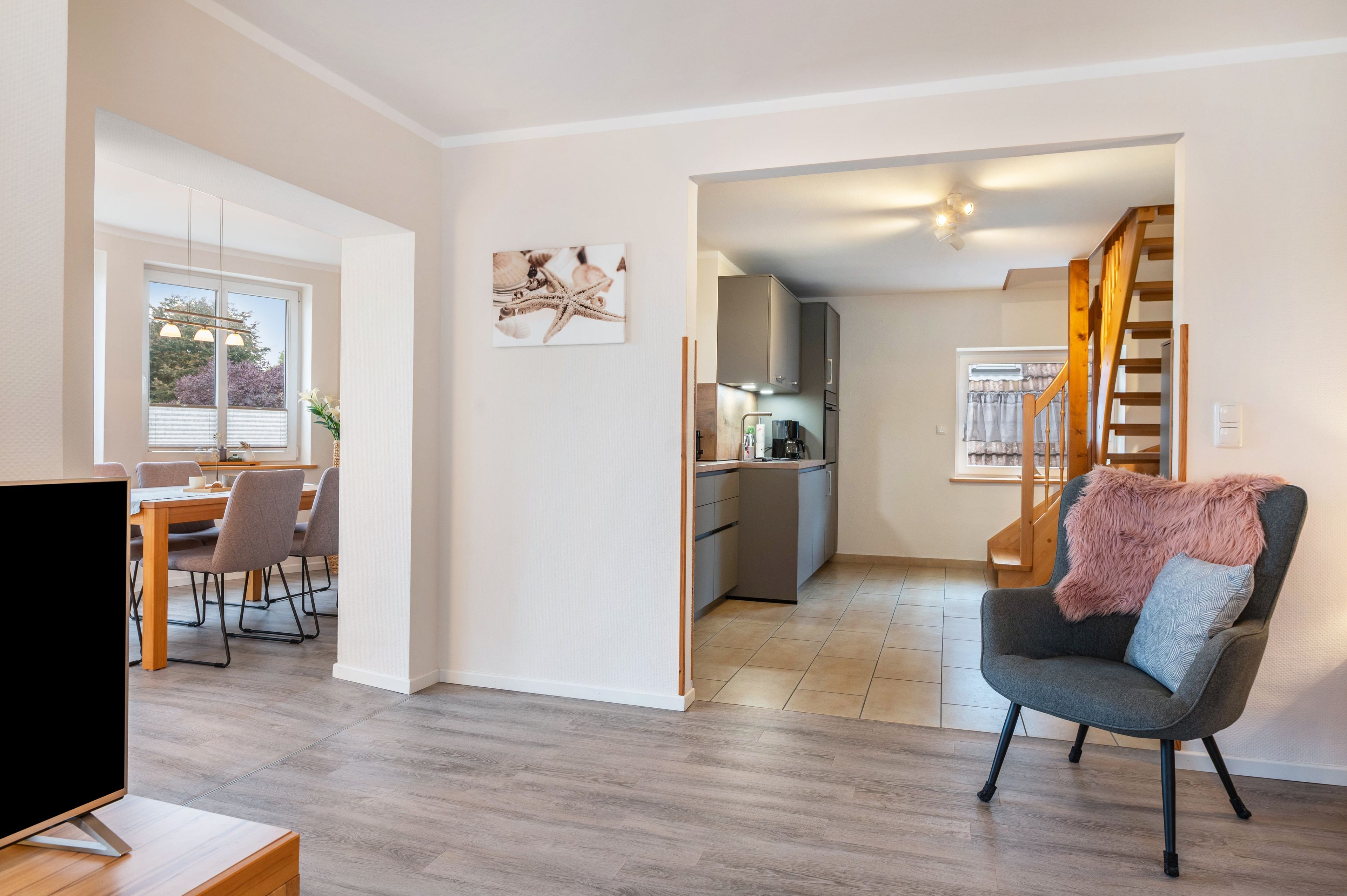 Ein modernes Wohnzimmer mit grauem Sofa, einem Essbereich mit Tisch und Stühlen, einer Küche mit eingebautem Ofen und Schränken sowie einer Treppe, die in eine andere Ebene führt.