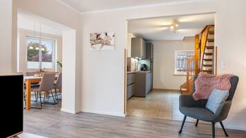 Ein modernes Wohnzimmer mit grauem Sofa, einem Essbereich mit Tisch und Stühlen, einer Küche mit eingebautem Ofen und Schränken sowie einer Treppe, die in eine andere Ebene führt.