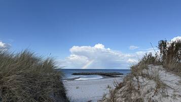 Ein Strandweg führt zum Meer, in der Ferne ist ein Regenbogen zu sehen.