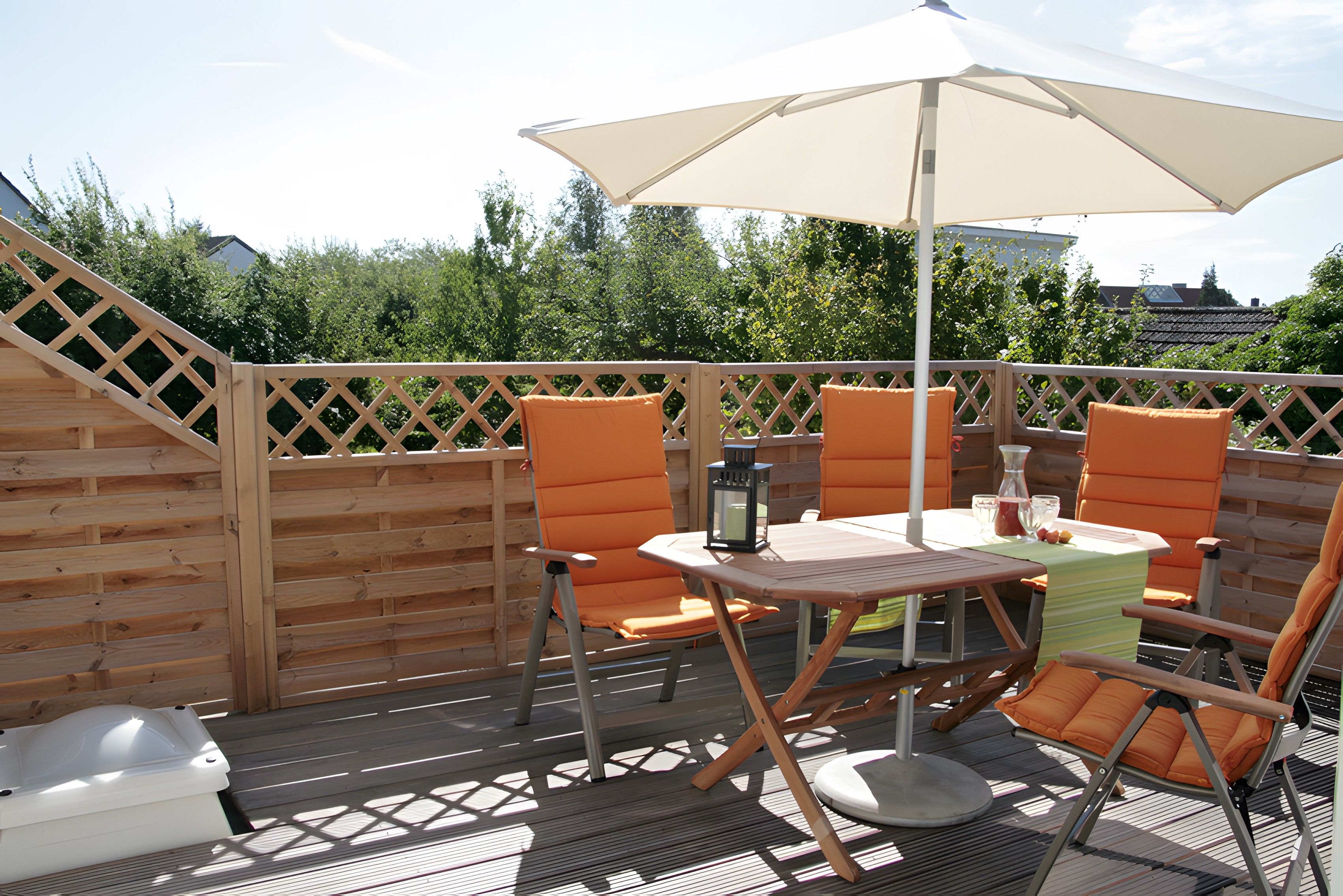 Eine Terrasse im Freien mit Holzboden, einem Tisch, vier Stühlen und einem großen Sonnenschirm.