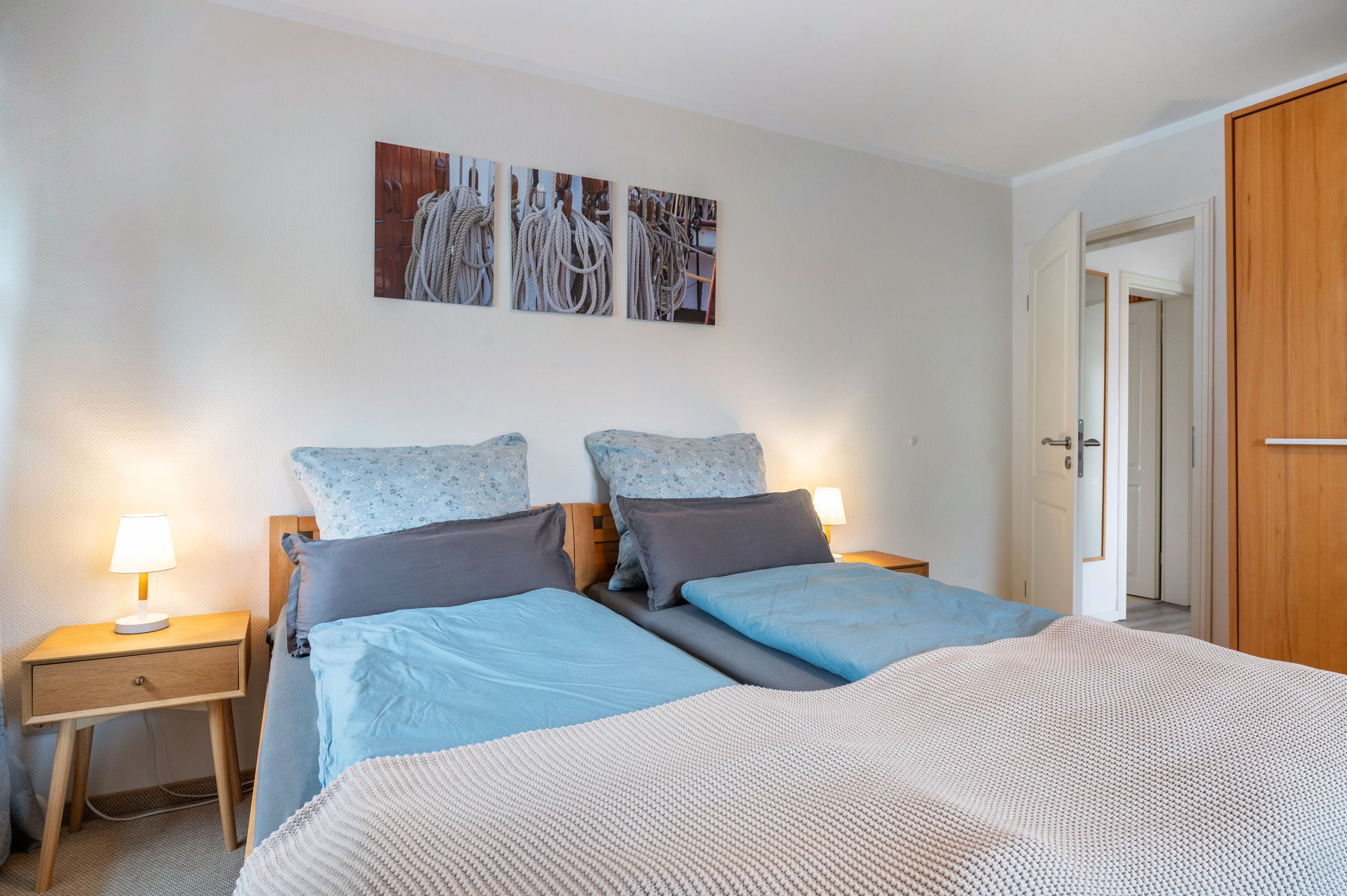 Ein Hotelzimmer mit einem Doppelbett, zwei Nachttischen mit Lampen, einem Holzschrank und einer Wand mit maritimer Dekoration.