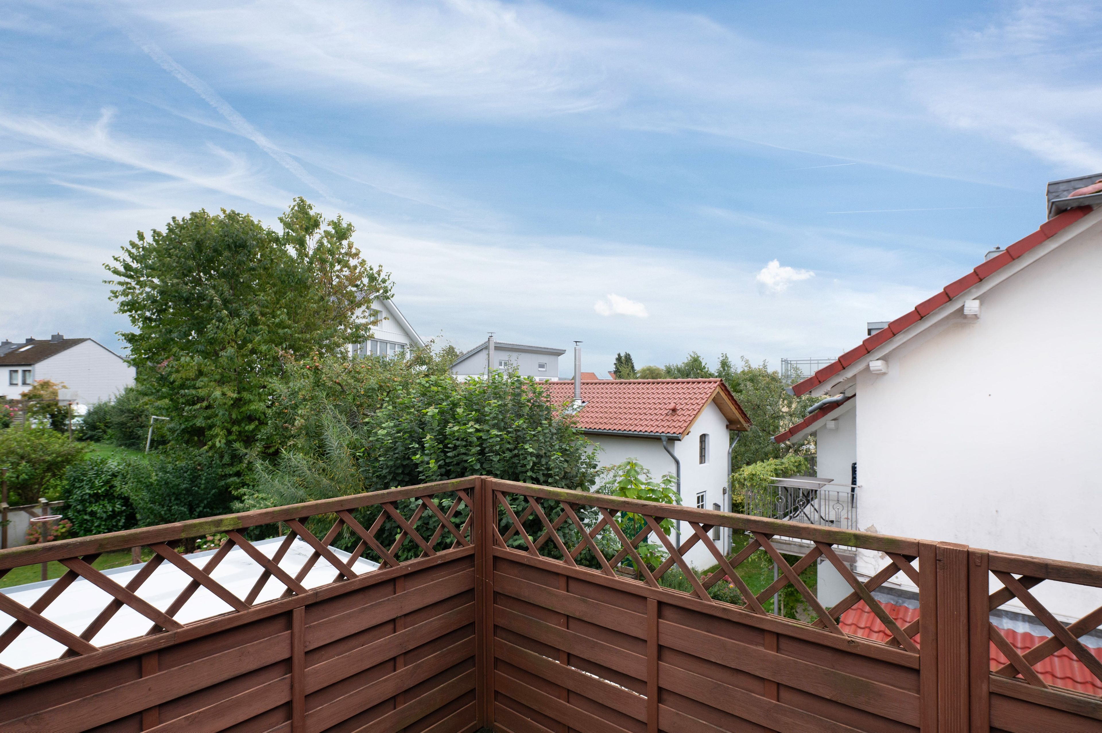 Ein Wohngebiet mit Holzzaun, einem Haus mit roten Ziegeldach und üppiger Bepflanzung.