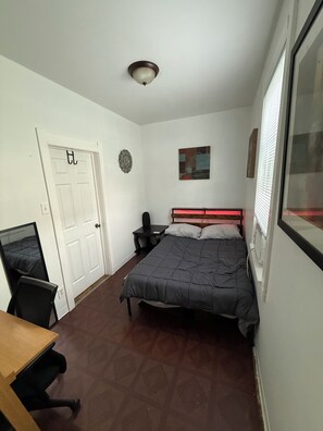 Ein Schlafzimmer mit einem Bett, einem Schreibtisch, einem Stuhl, einer Tür und einem Fenster.